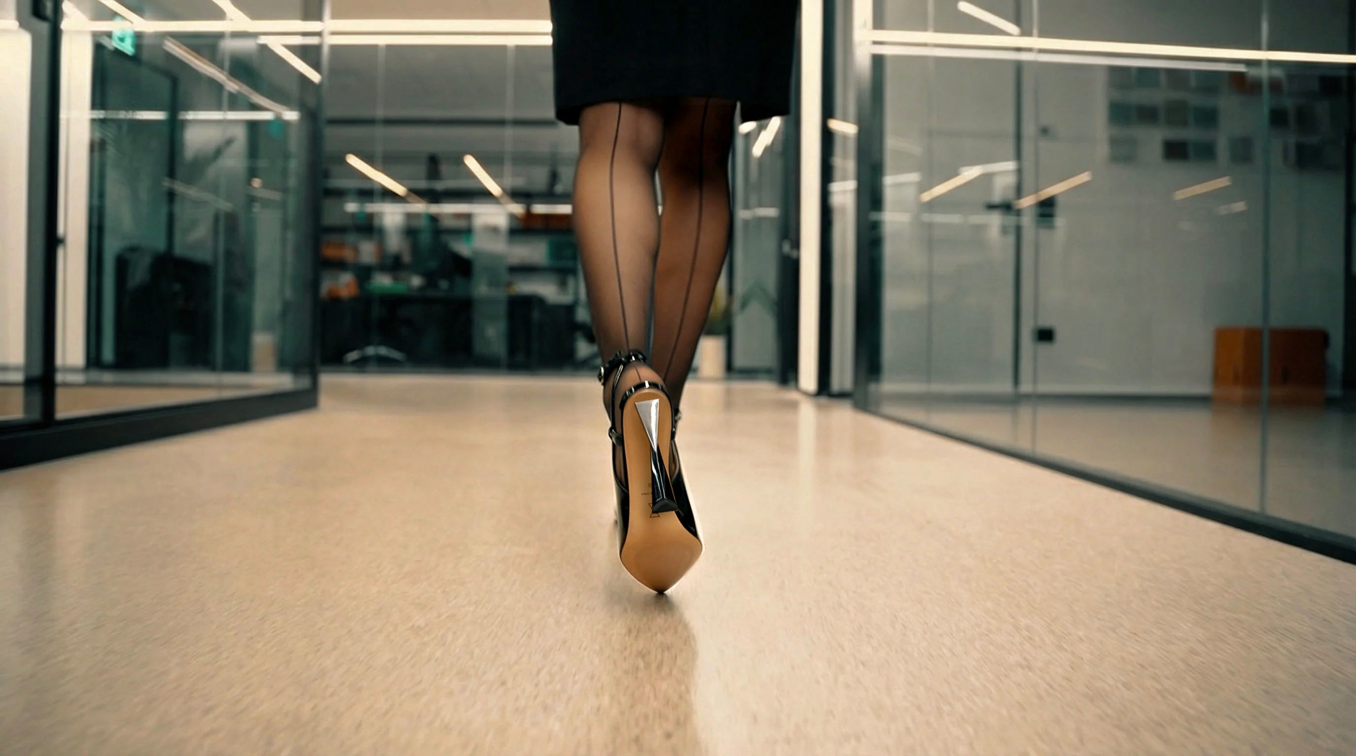 Woman walking in Vanessa Nardulli black heels down modern hallway, rear view