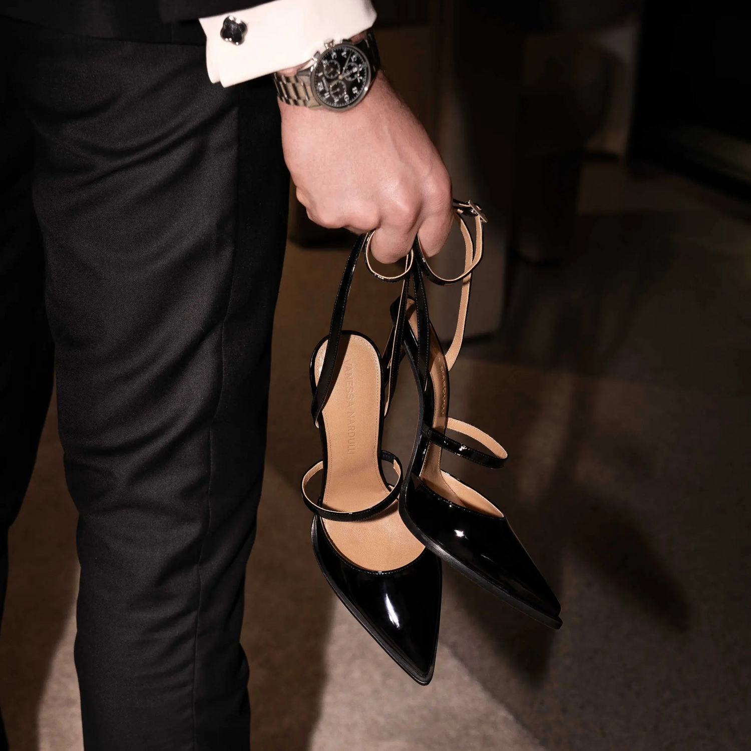 Black patent leather heels with geometric heel held by man in tailored suit